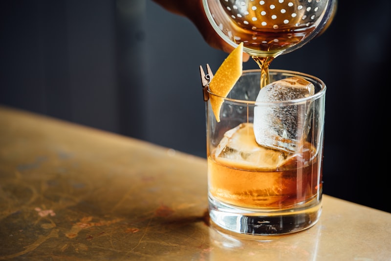 Ein Getränk wird in ein Glas mit großer Eiswürfel und Zitrusgarnitur gegossen.