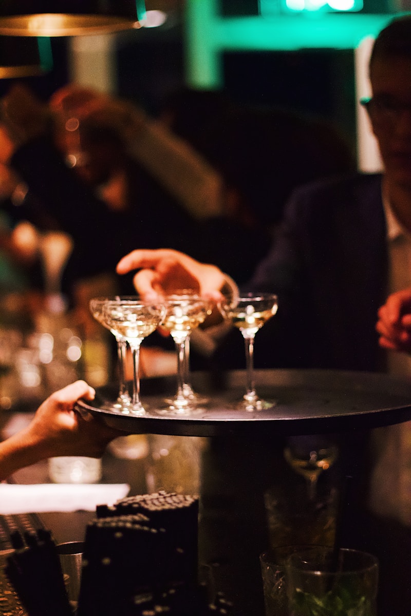 Person stellt Tablett mit Martini-Gläsern an einer Bar bereit.