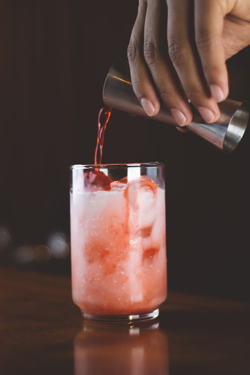 Person gießt roten Saft in ein Glas mit Eiswürfeln.