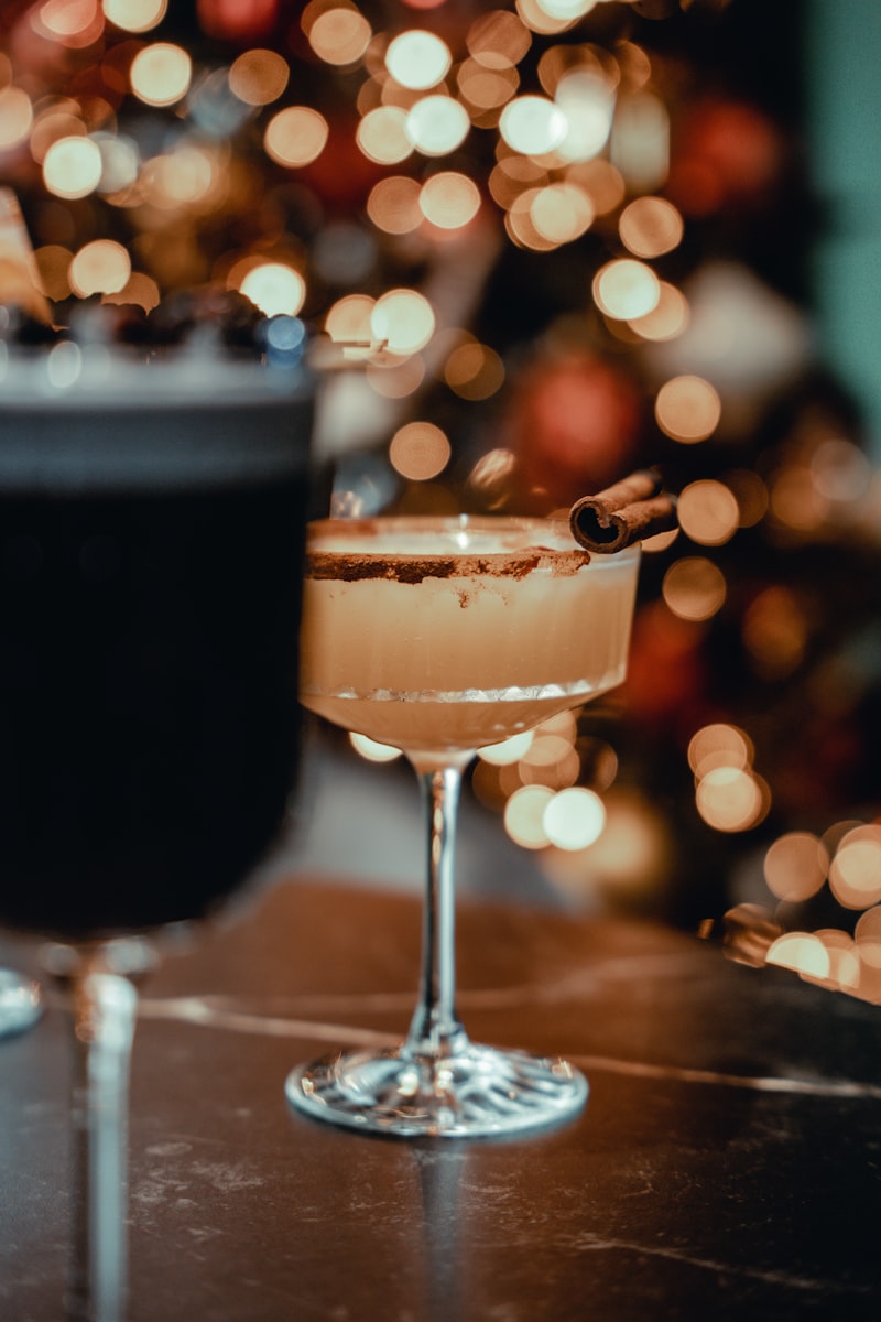 Ein Cocktailglas mit Zimtstange, verschwommene Lichter im Hintergrund.